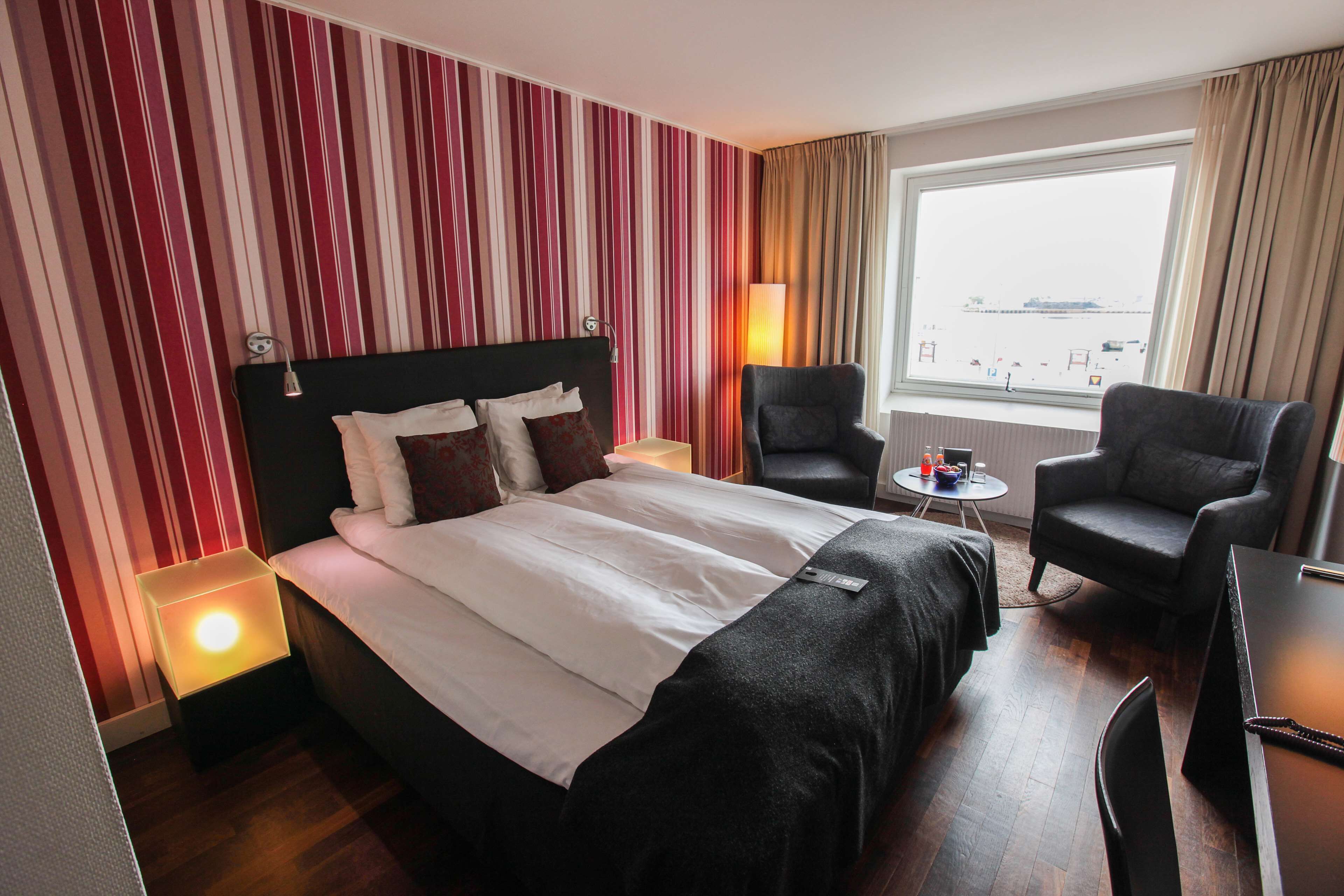 Ein Hotelzimmer mit einem großen Bett, zwei Sesseln, einem kleinen Tisch und einem Fenster mit Blick.