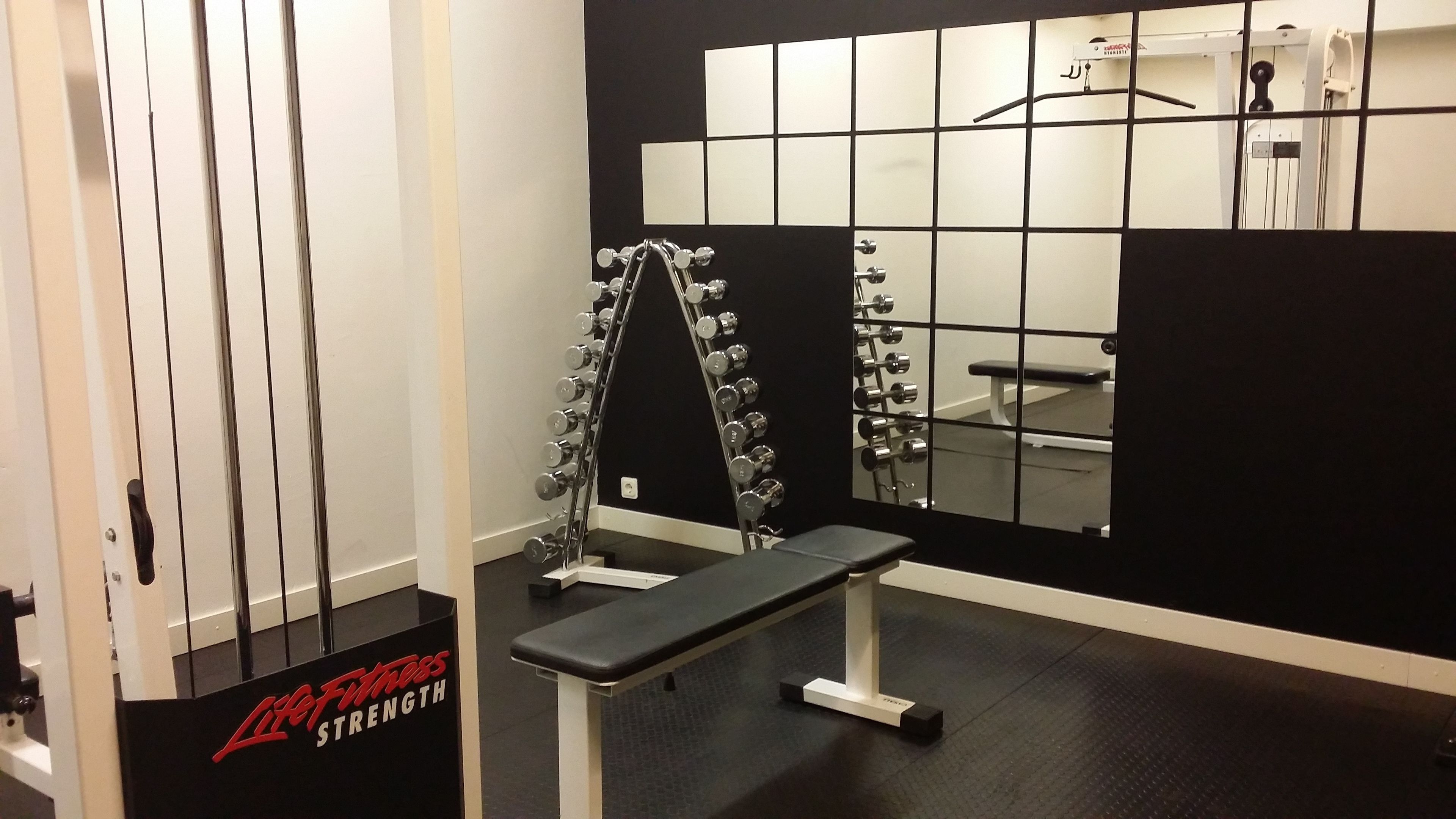 Une salle de sport équipée d’un banc, d’haltères et d’un miroir.
