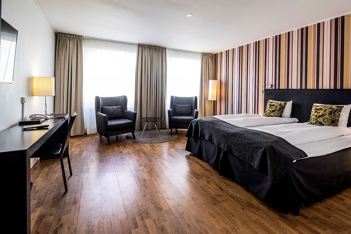 Habitación de hotel con cama, dos sillones, un escritorio y una lámpara.