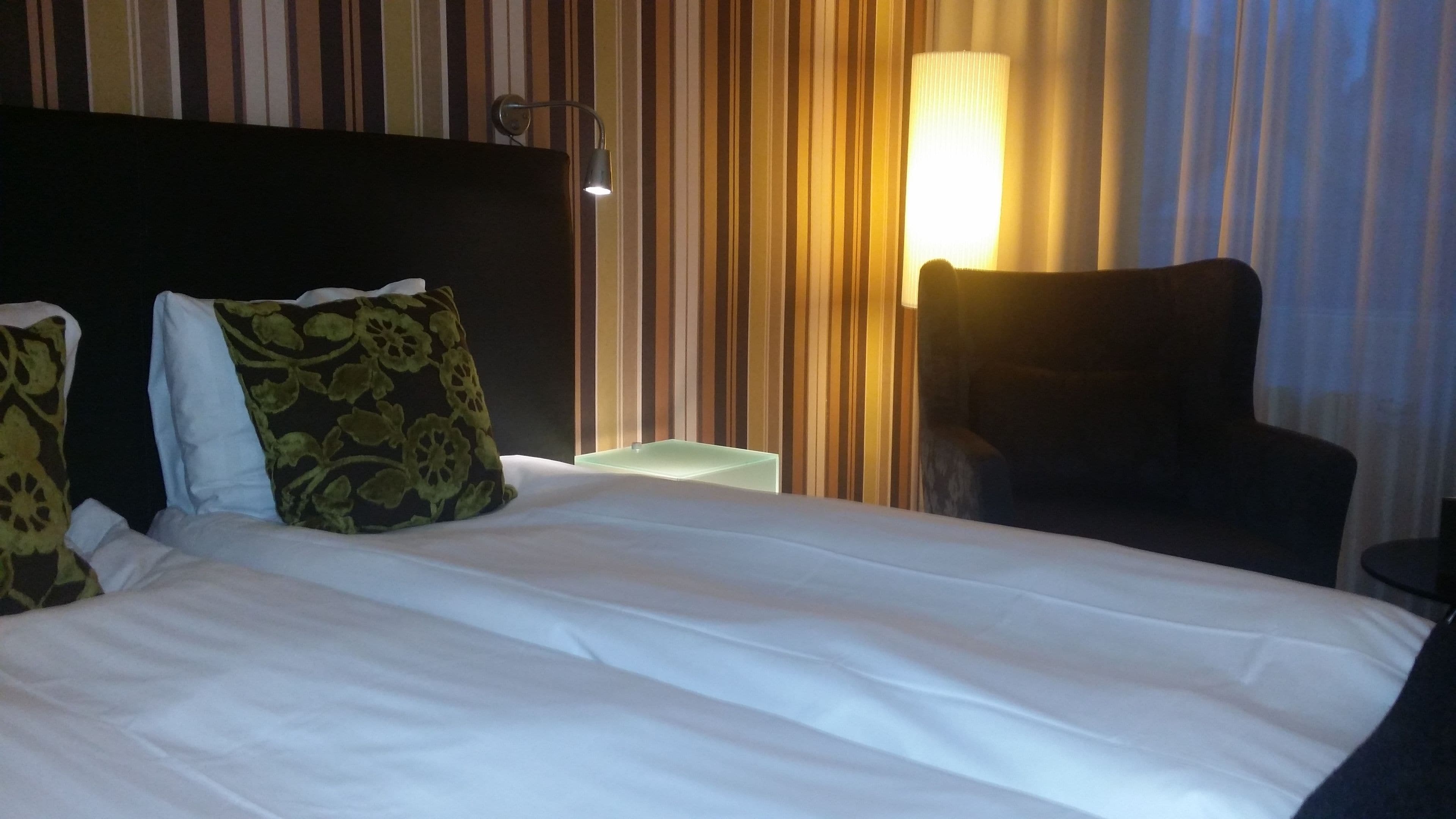 A hotel room with a bed, a chair, a nightstand, and a lamp.