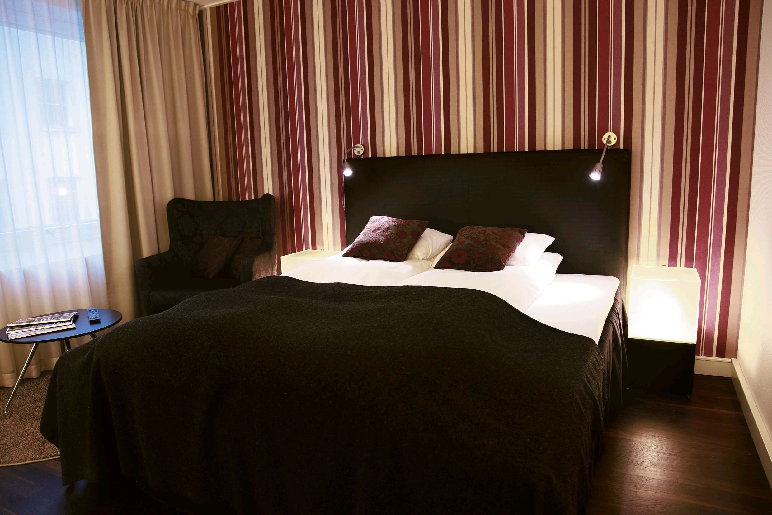Habitación de hotel con una cama grande, una silla, una mesita y una ventana con cortinas.