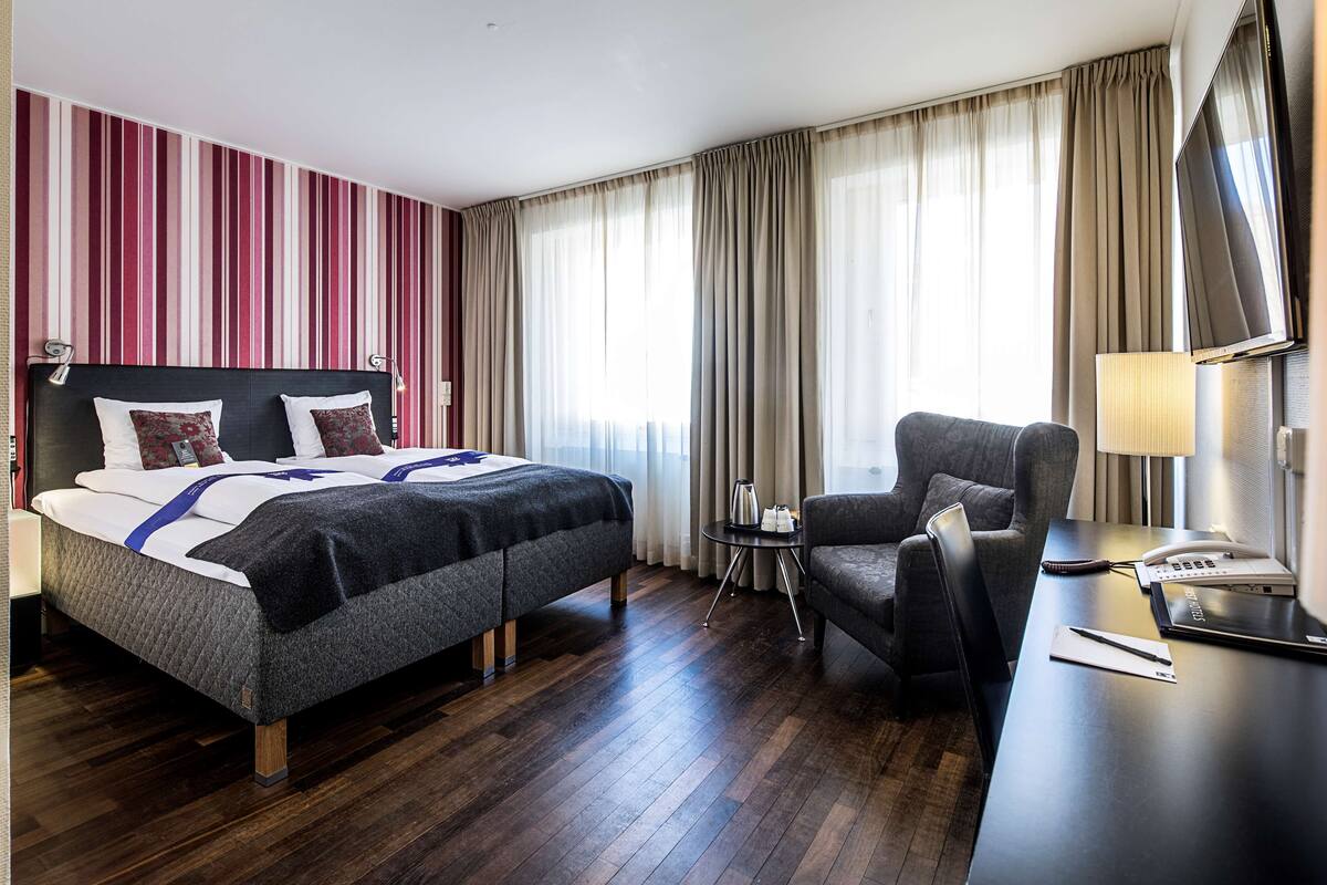 Habitación de hotel con una cama grande, un escritorio, una silla, un televisor y una pequeña mesa con lámpara.
