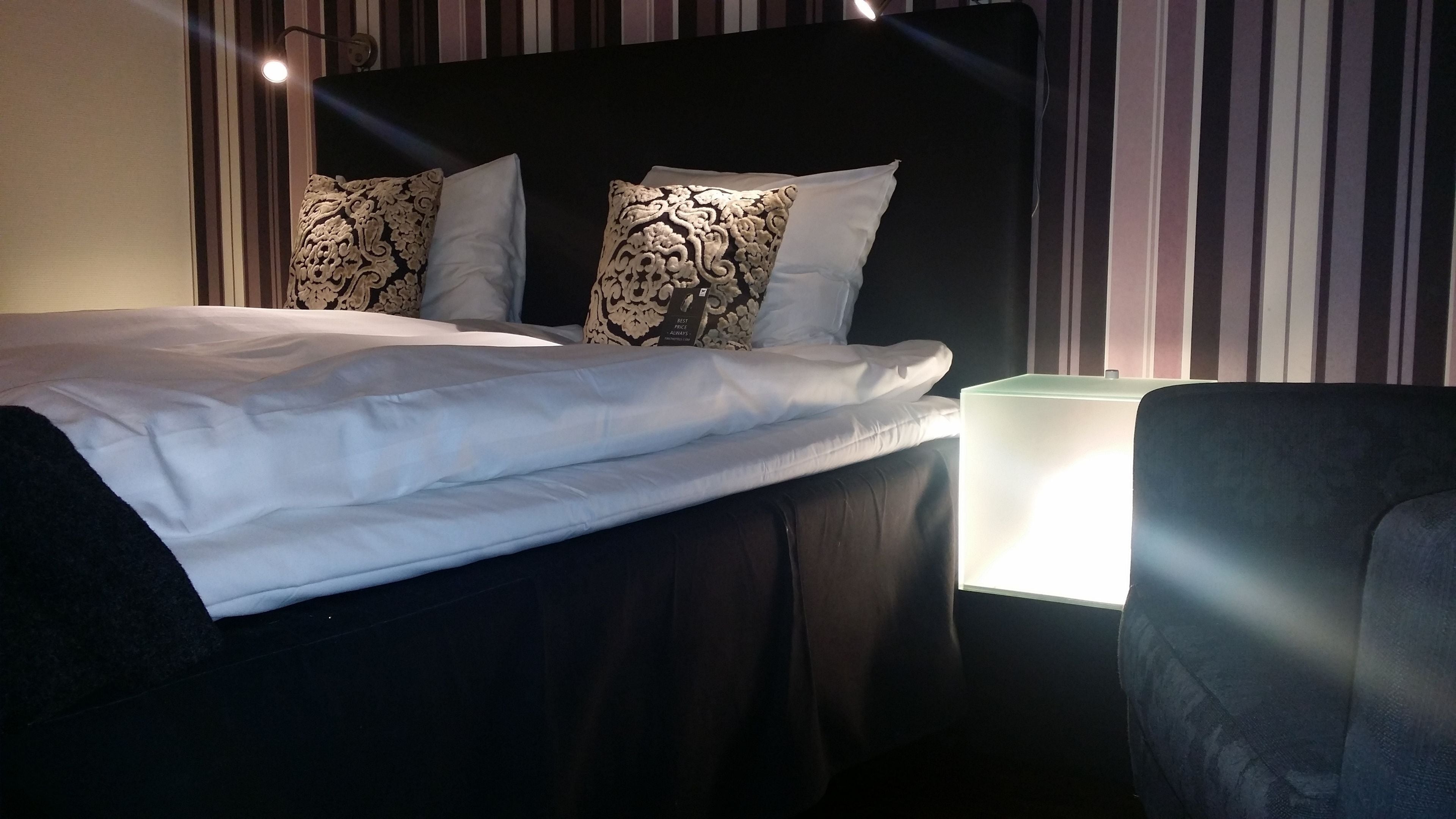 Un lit bien fait, avec du linge de lit blanc et des coussins décoratifs, une lampe de chevet et une chaise.