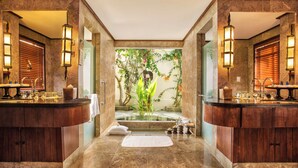 A luxurious bathroom with a central bathtub, wooden cabinets, and two side sinks. - The Oberoi, Lombok (Tanjung)