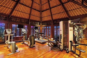 A gym with various exercise equipment, large windows, and a wooden ceiling. - The Oberoi, Lombok (Tanjung)