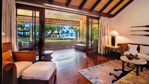 A spacious room with a wooden ceiling, a large window, and a view of a pool and palm trees. - The Oberoi, Lombok (Tanjung)