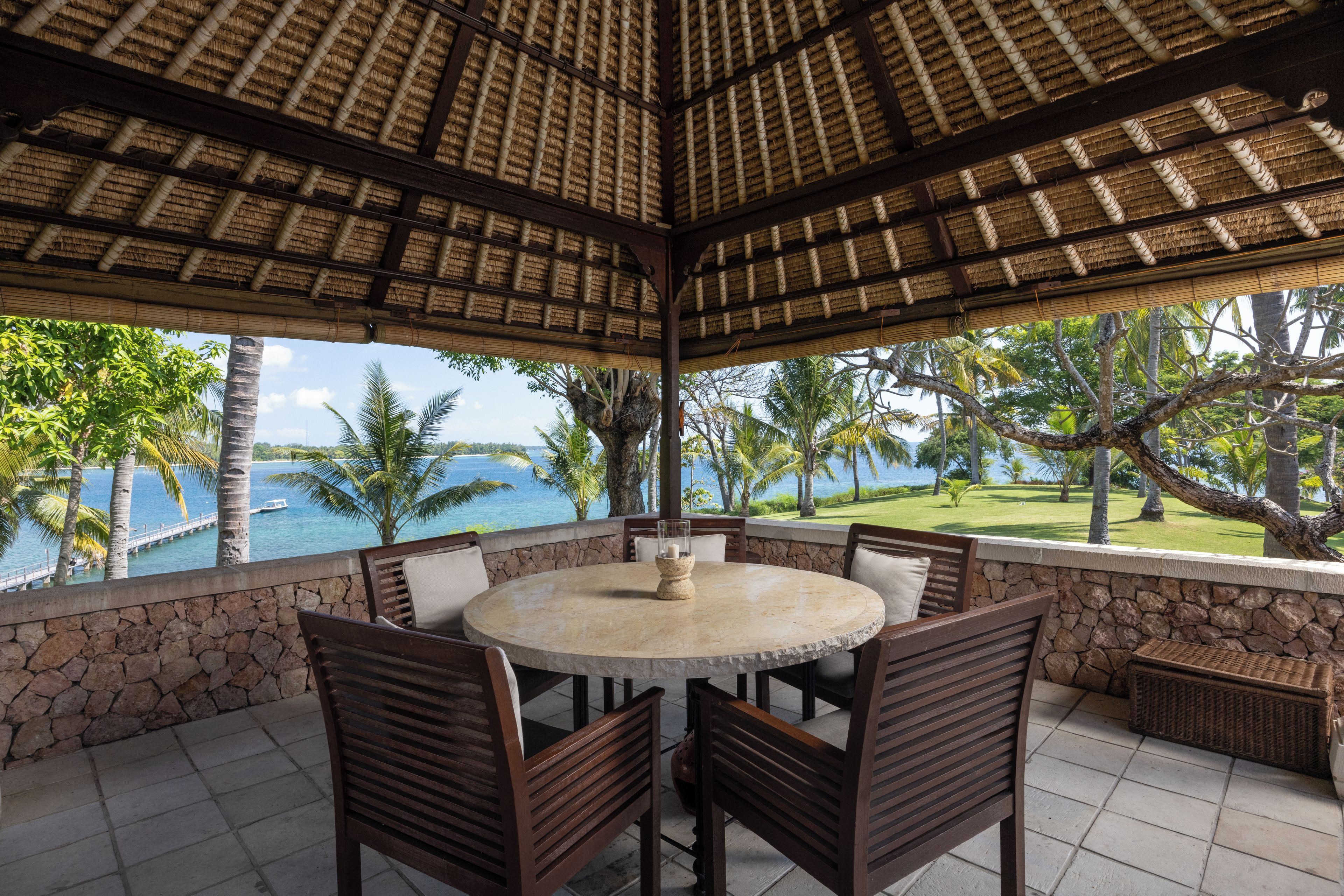 A covered outdoor seating area with a stone wall, a round table, and chairs.