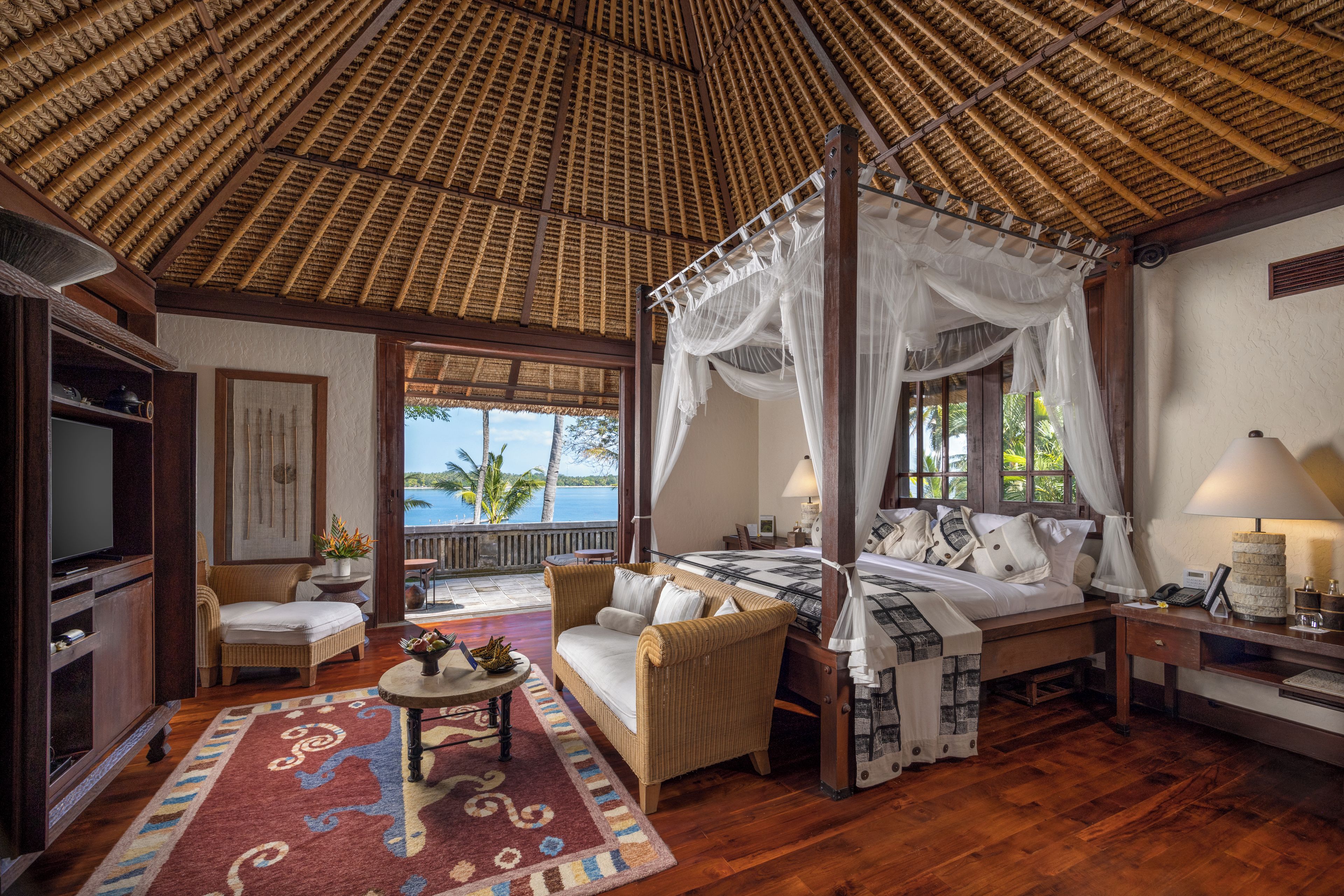 A room with a four-poster bed, a television, a dining table, and a view of the sea.