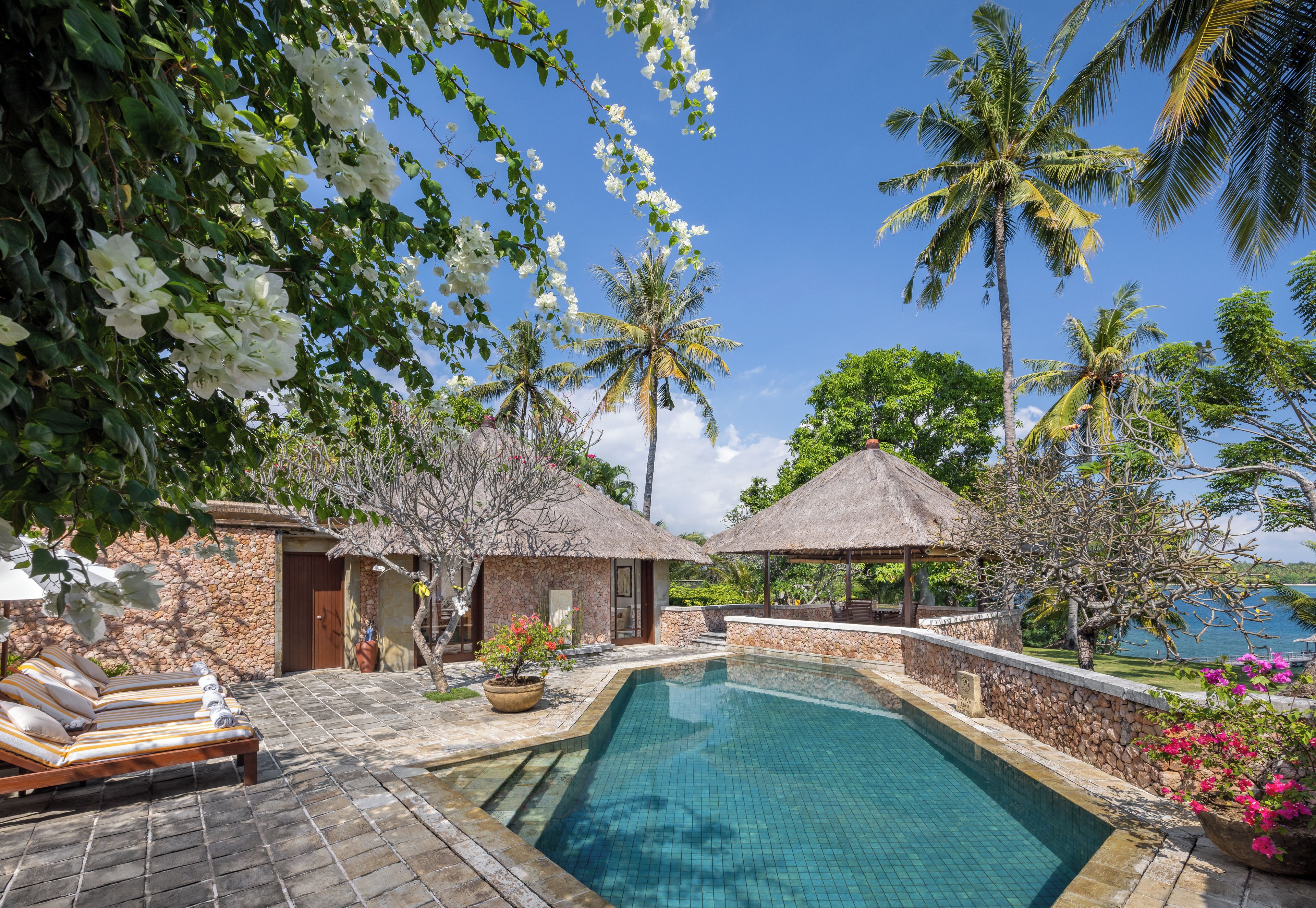 A pool area with a stone deck, lounge chairs, and a view of the ocean.
