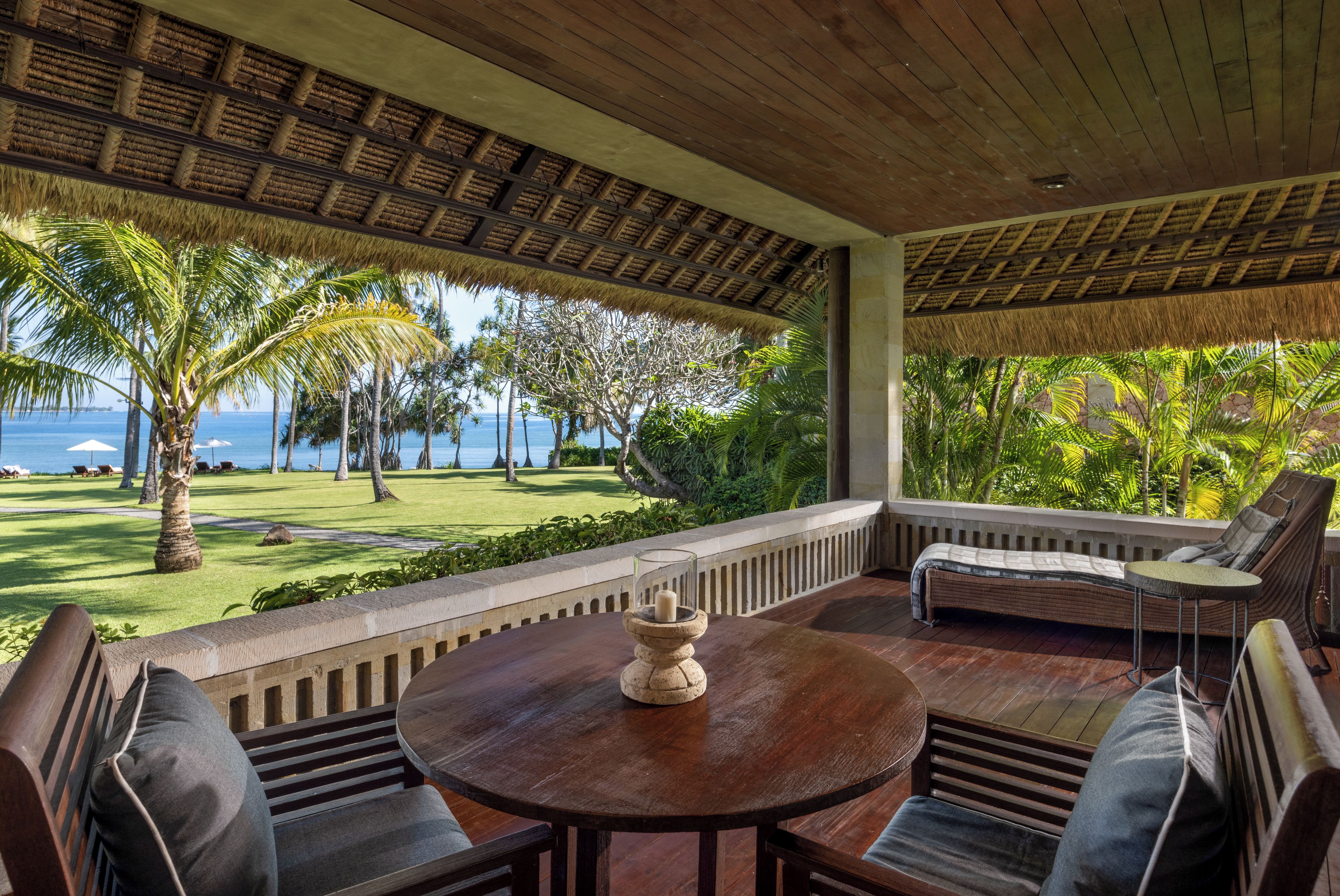 A covered outdoor seating area with a view of the ocean, a thatched roof, and a well-maintained lawn.