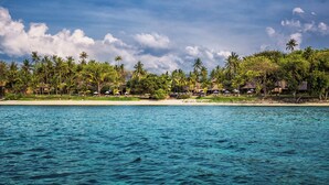 A beach resort with a clear view of the ocean, palm trees, and thatched-roof huts. - The Oberoi, Lombok (Tanjung)