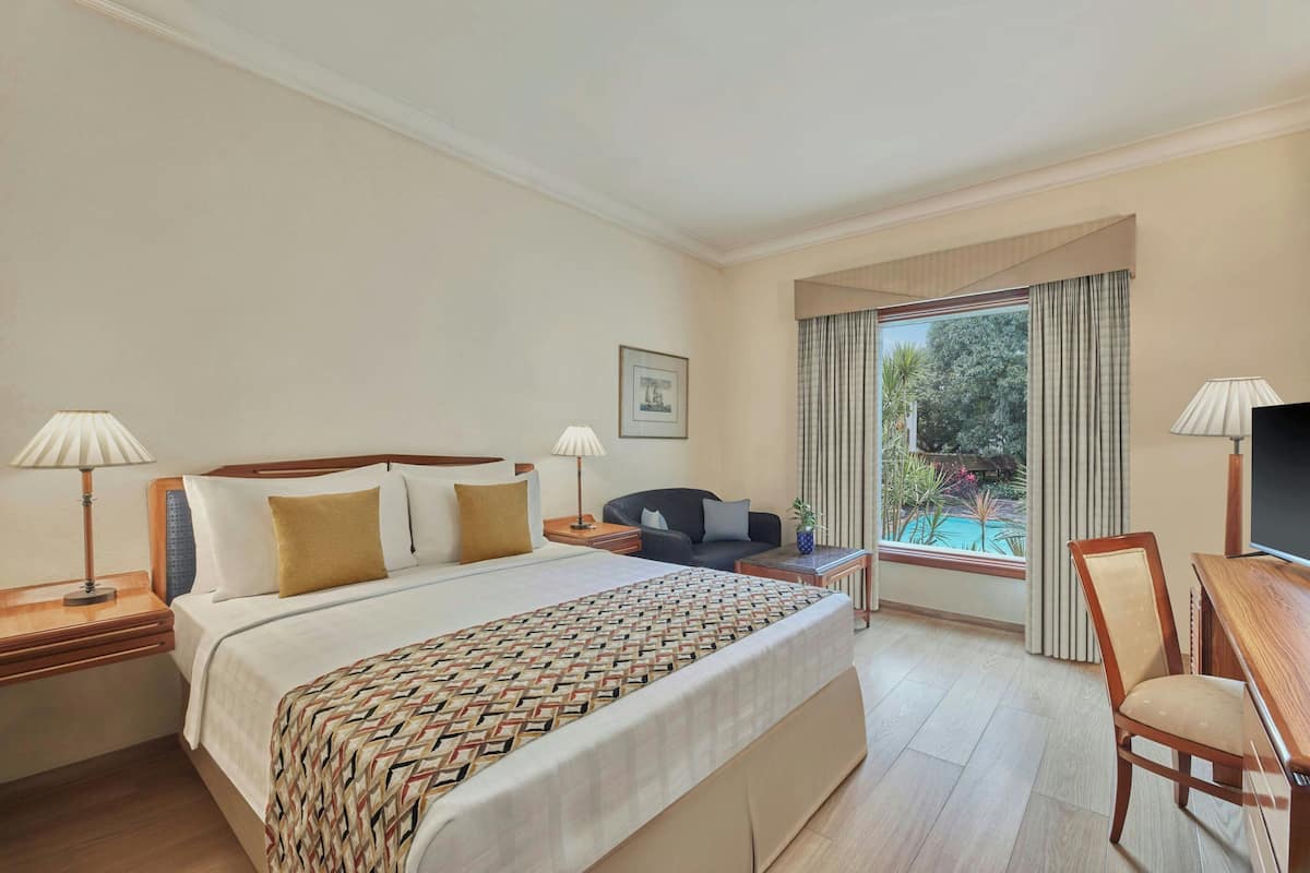 A hotel room with a large bed, a desk, a chair, and a TV.