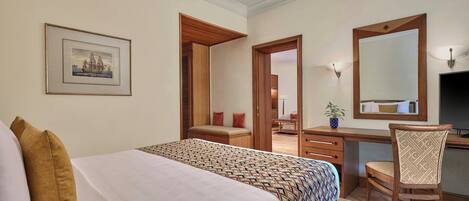 A hotel room with a bed, a desk, a chair, a mirror, and a framed picture on the wall.