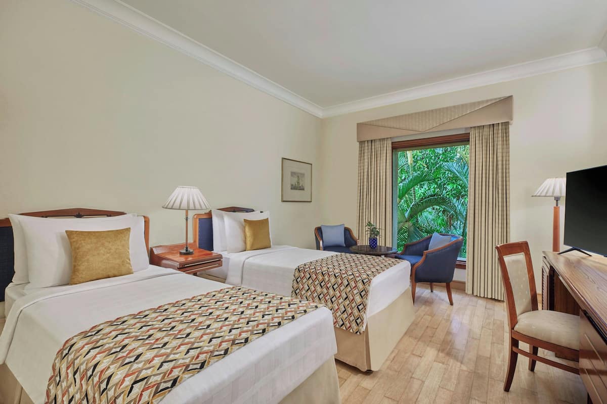 Ein Hotelzimmer mit zwei Betten, einem Schreibtisch, einem Sessel, einem Fernseher und einem Fenster mit Vorhängen.