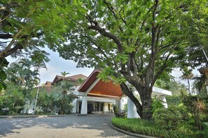 A building with a red roof and white walls, surrounded by lush greenery and palm trees.