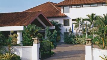 A white building with a tiled roof, surrounded by palm trees and a paved entrance.