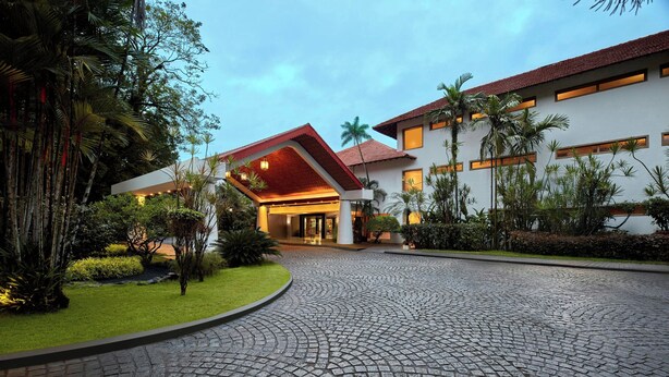 A hotel entrance with a cobblestone driveway, a red-roofed building, and surrounding greenery.