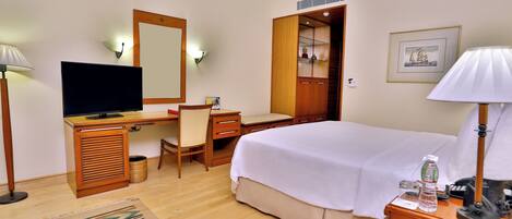 A hotel room with a bed, desk, chair, television, and a wardrobe.