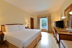 A hotel room with a large bed, a desk with a television, a mirror, and a window with curtains.