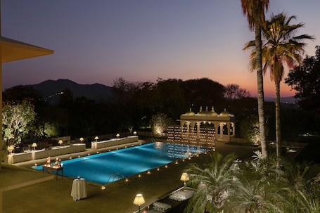 A swimming pool with surrounding tables and chairs, a gazebo, and palm trees.