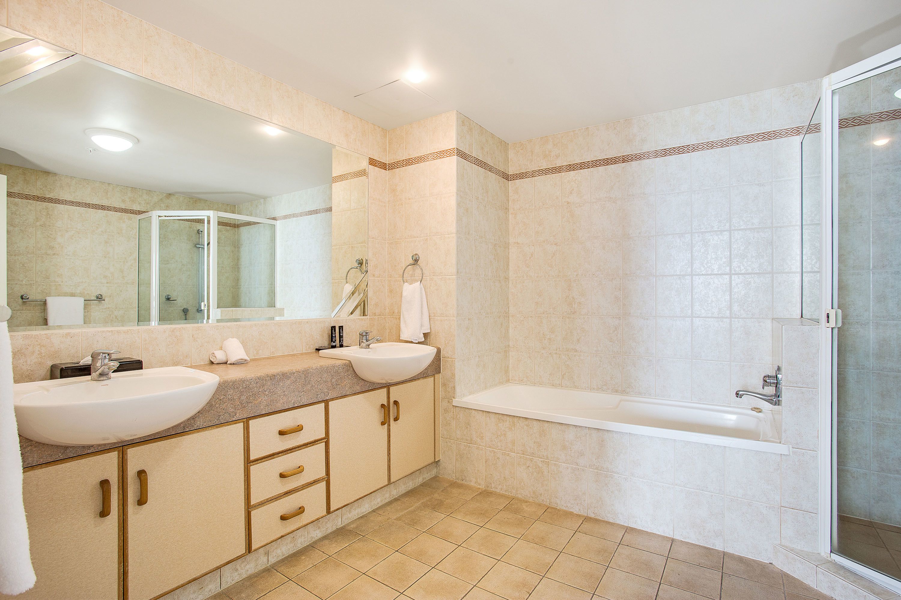 Un baño moderno con dos lavabos, un espejo grande, una bañera y una ducha con mampara de vidrio.