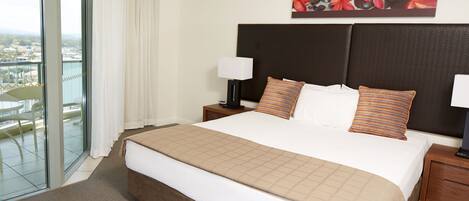A hotel room with a large bed, two bedside tables with lamps, a view through a sliding glass door, and a painting above the bed.