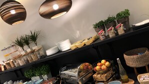 A buffet setup with various food items, including fruits, cheeses, and condiments, arranged on a table with overhead lighting. - Villa Ozone (Sopot)