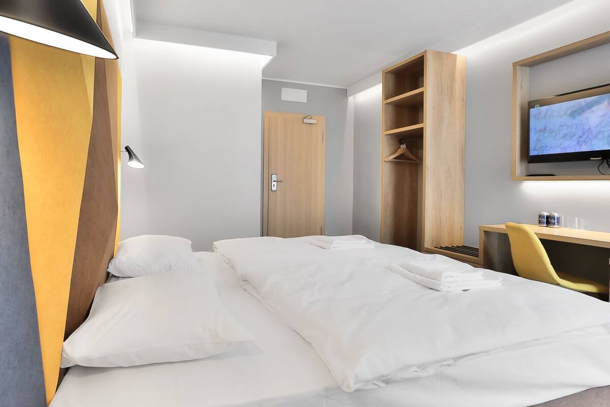A hotel room with a bed, a desk, a TV, and a wardrobe.