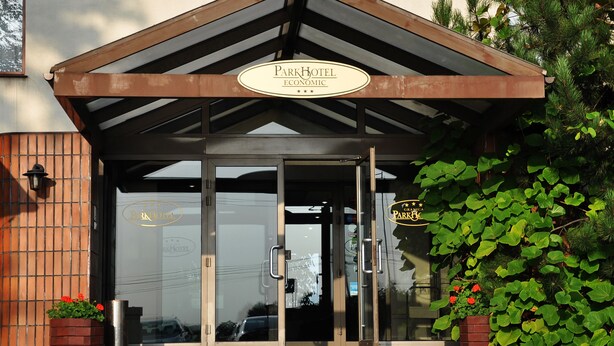 A hotel entrance with a glass door, a sign above the door, and a small planter with flowers. - Parkhotel Economic (Wielka Wies)