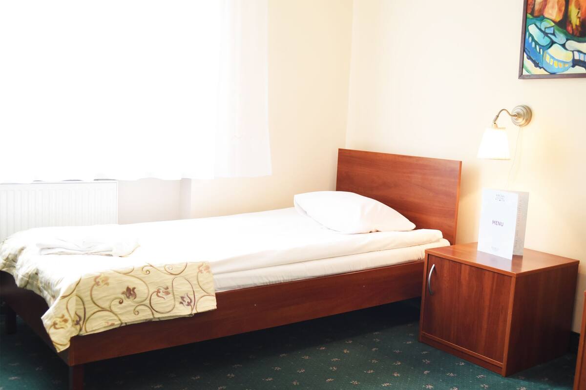 A neatly made bed with a wooden headboard, a bedside table with a lamp, and a sign indicating a menu.
