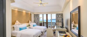 A hotel room with two beds, a desk, a chair, a television, and a large window offering a view of the sea.