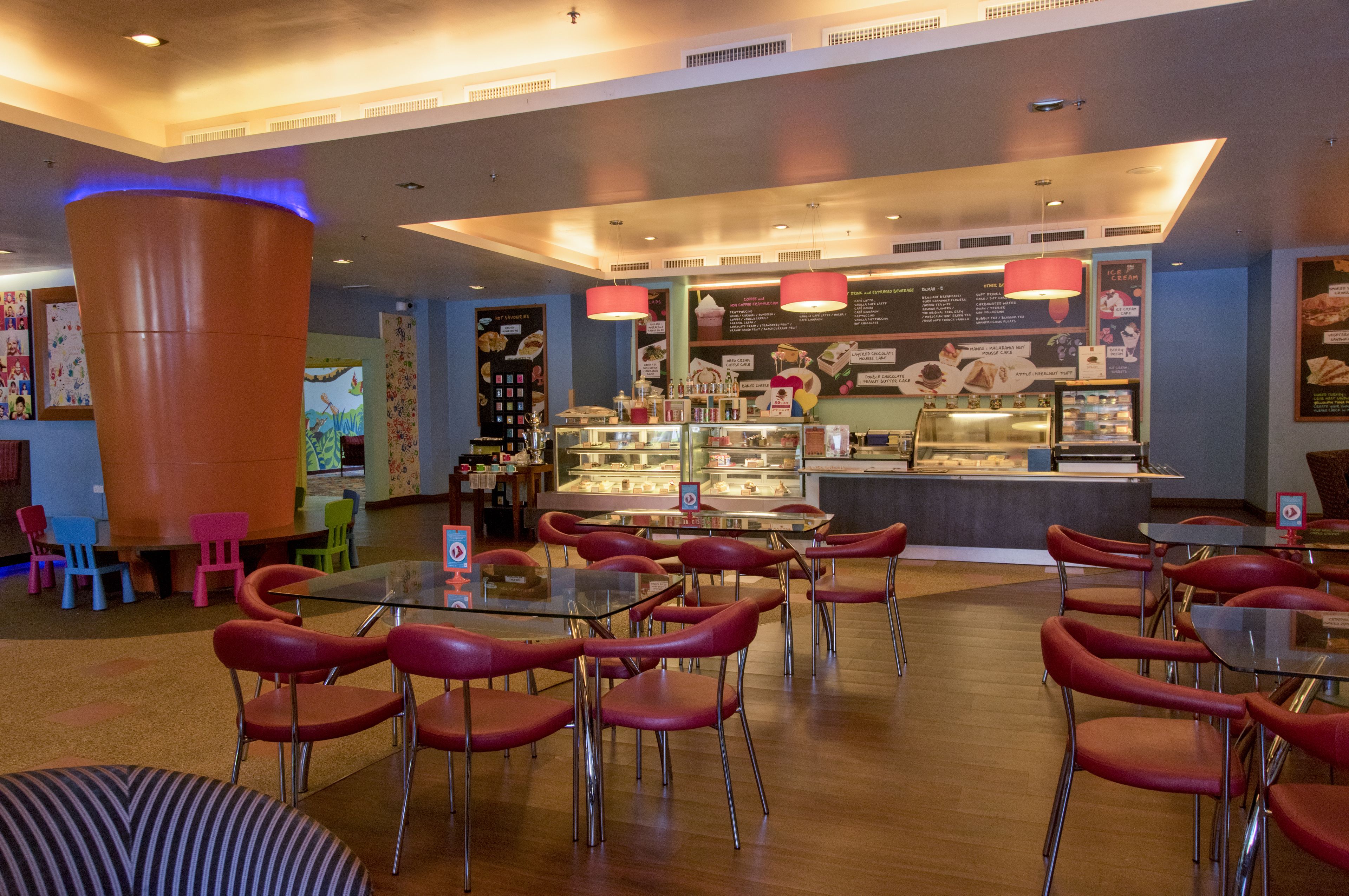 A restaurant with red chairs, a glass table, and a dessert display.