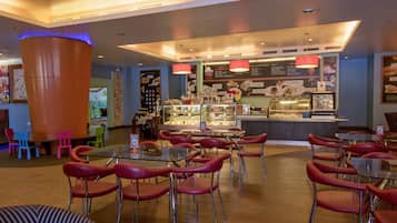 A restaurant with red chairs, a glass table, and a dessert display.