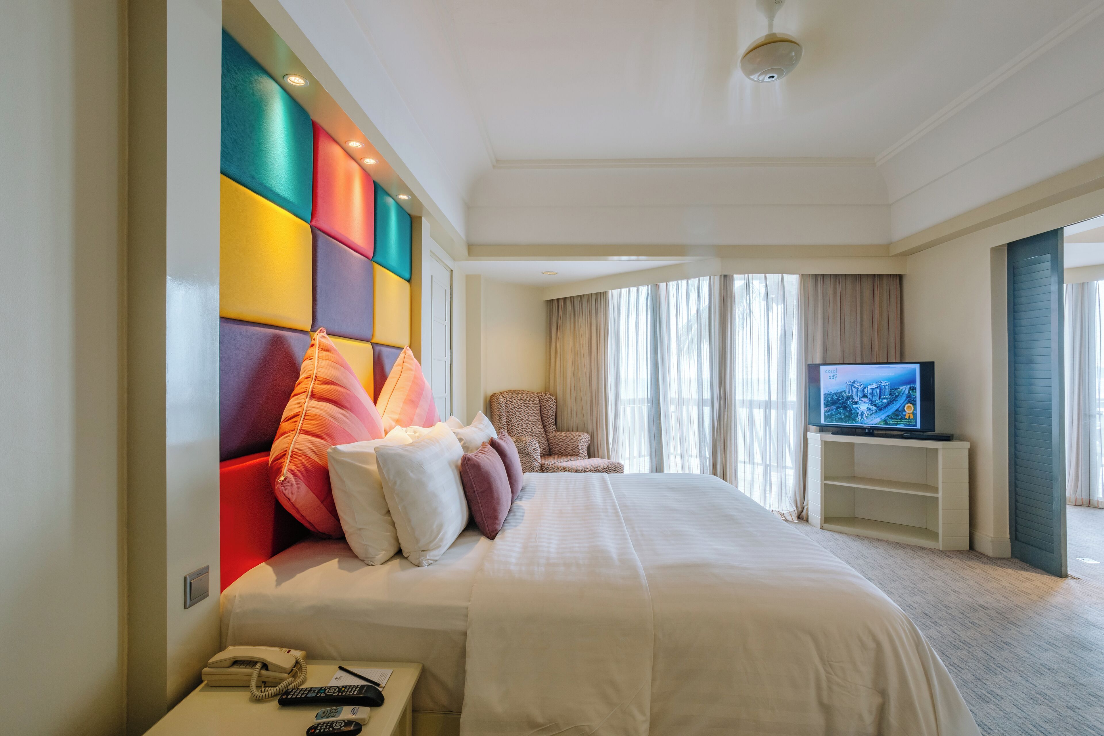 A hotel room with a large bed, a television, a chair, and a phone on the side table.