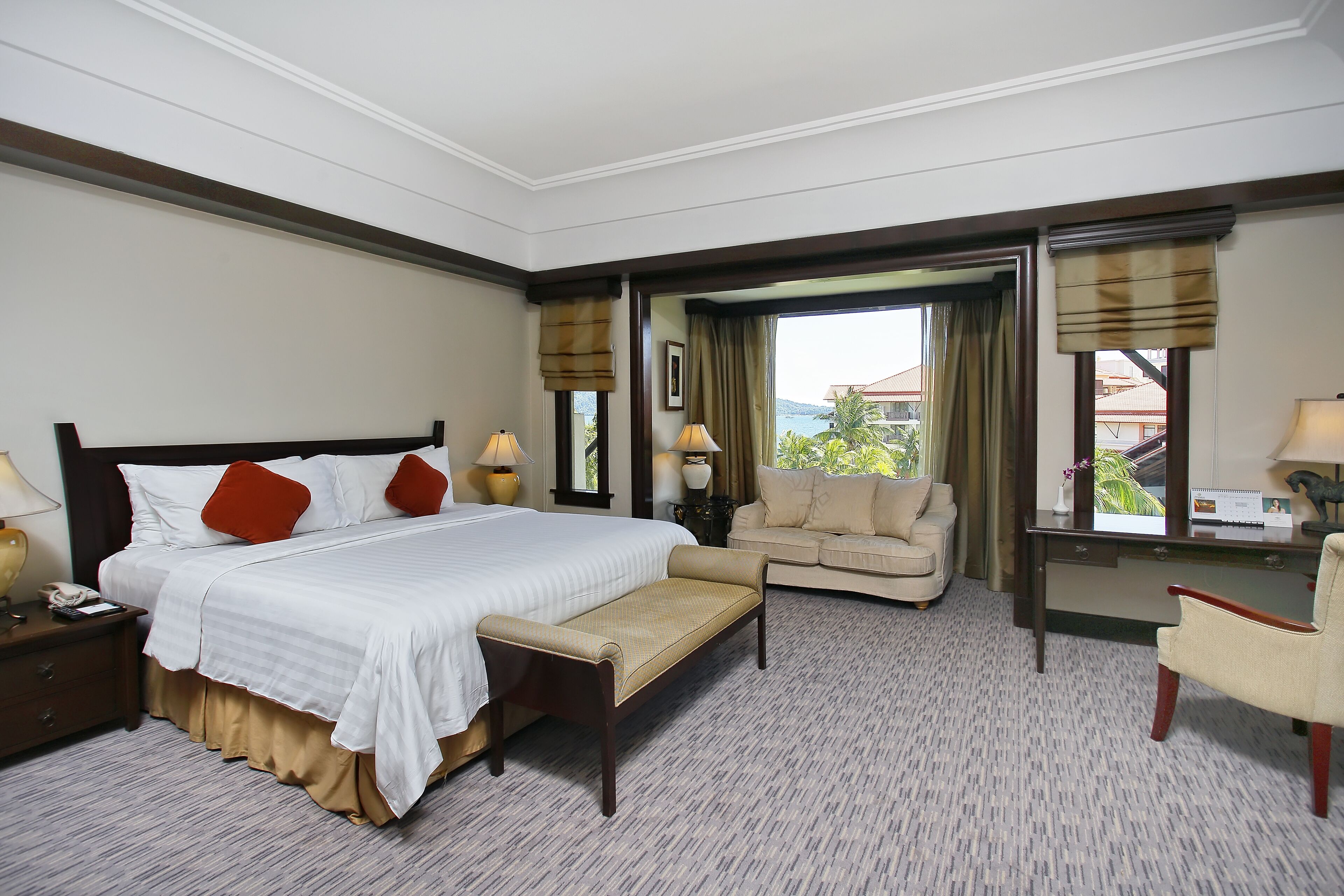 A hotel room with a large bed, a sofa, a desk, and a chair. There is a window with a view of the outside.