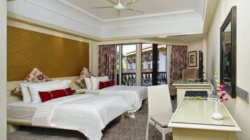A hotel room with two beds, a desk, a chair, a ceiling fan, and a view of the outside balcony.