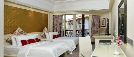 A hotel room with two beds, a desk, a chair, a ceiling fan, and a view of the outside balcony.