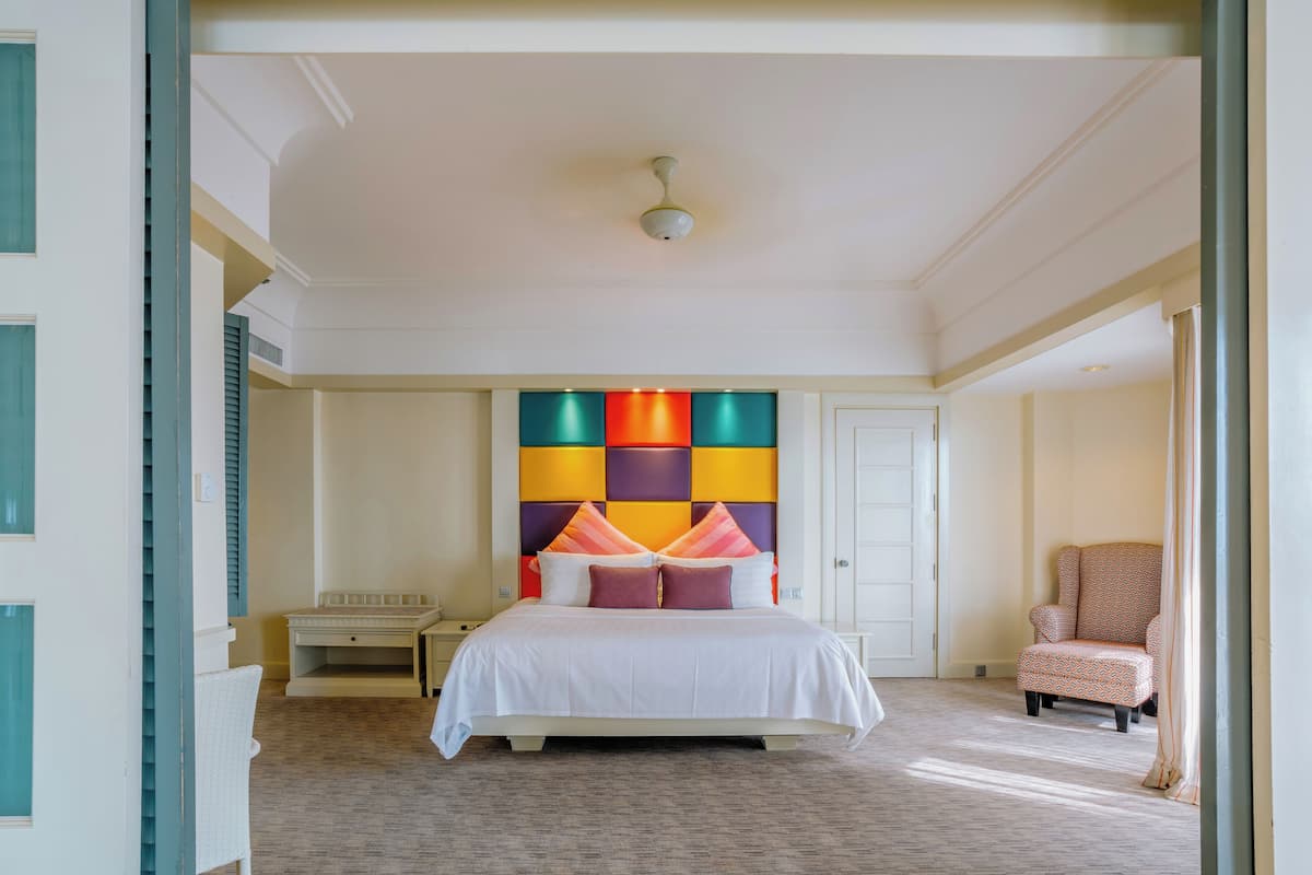 A hotel room with a large bed, a nightstand, a chair, and a colorful headboard.