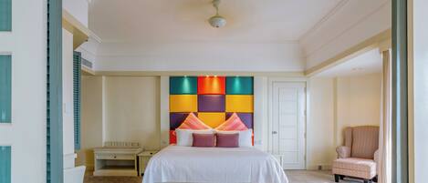 Una camera d'albergo con un letto grande, un comodino, una sedia e una testiera colorata.