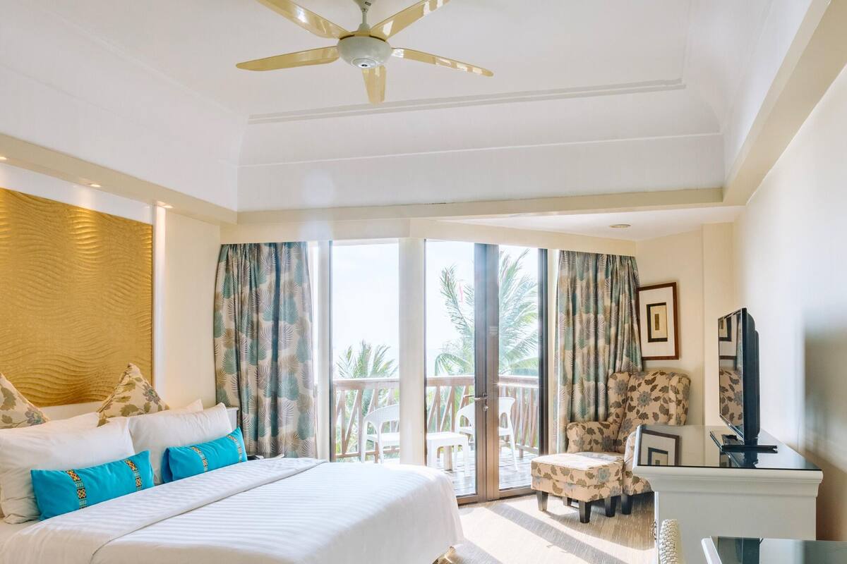 A hotel room with a bed, a TV, a chair, and a balcony with a view.