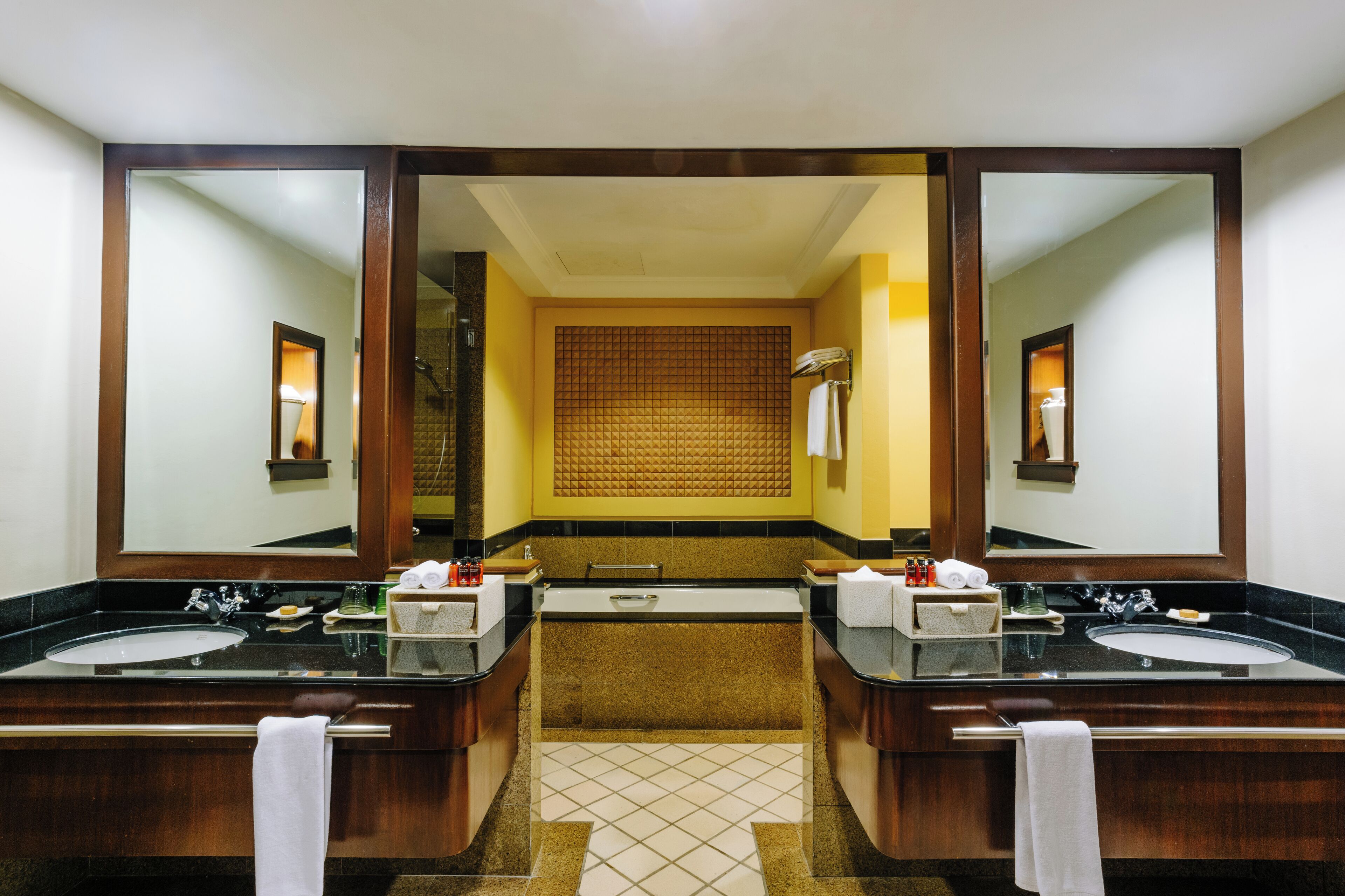 A hotel bathroom with two sinks, a bathtub, and a large mirror.