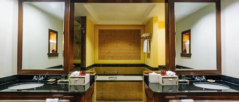 A hotel bathroom with two sinks, a bathtub, and a large mirror.