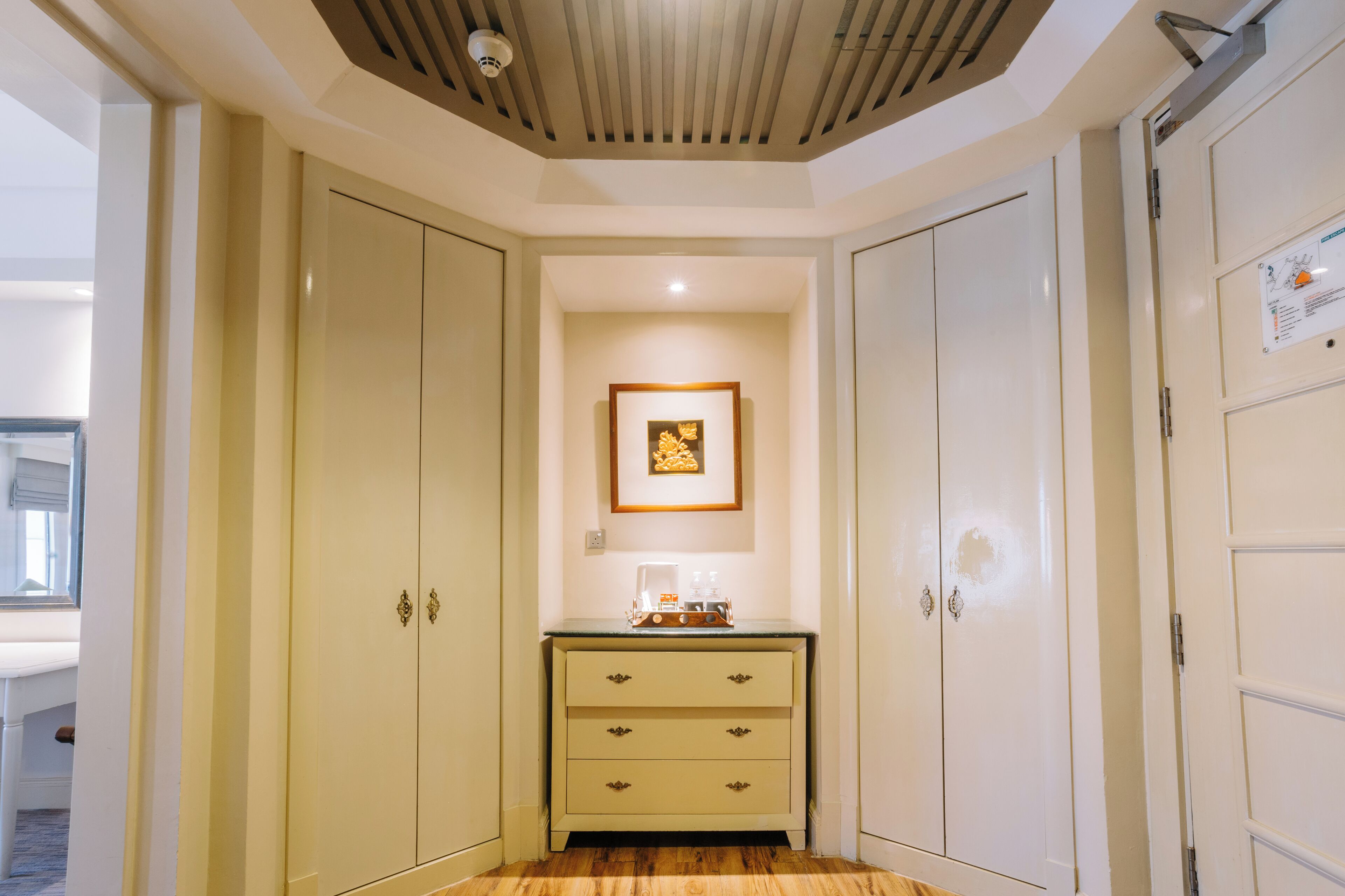 A narrow hallway with a wooden floor, a small table with a coffee maker, and a framed picture on the wall.