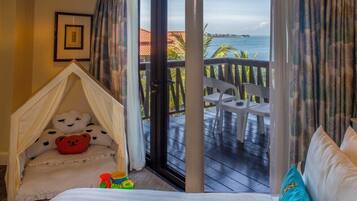 A bedroom with a bed, a white canopy bed, a balcony with a view of the sea, and a chair.