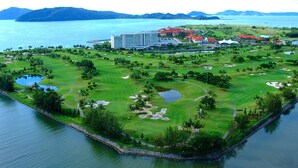 An aerial view of a golf course with a large hotel, water bodies, and lush greenery. - The Magellan Sutera Resort (Kota Kinabalu)