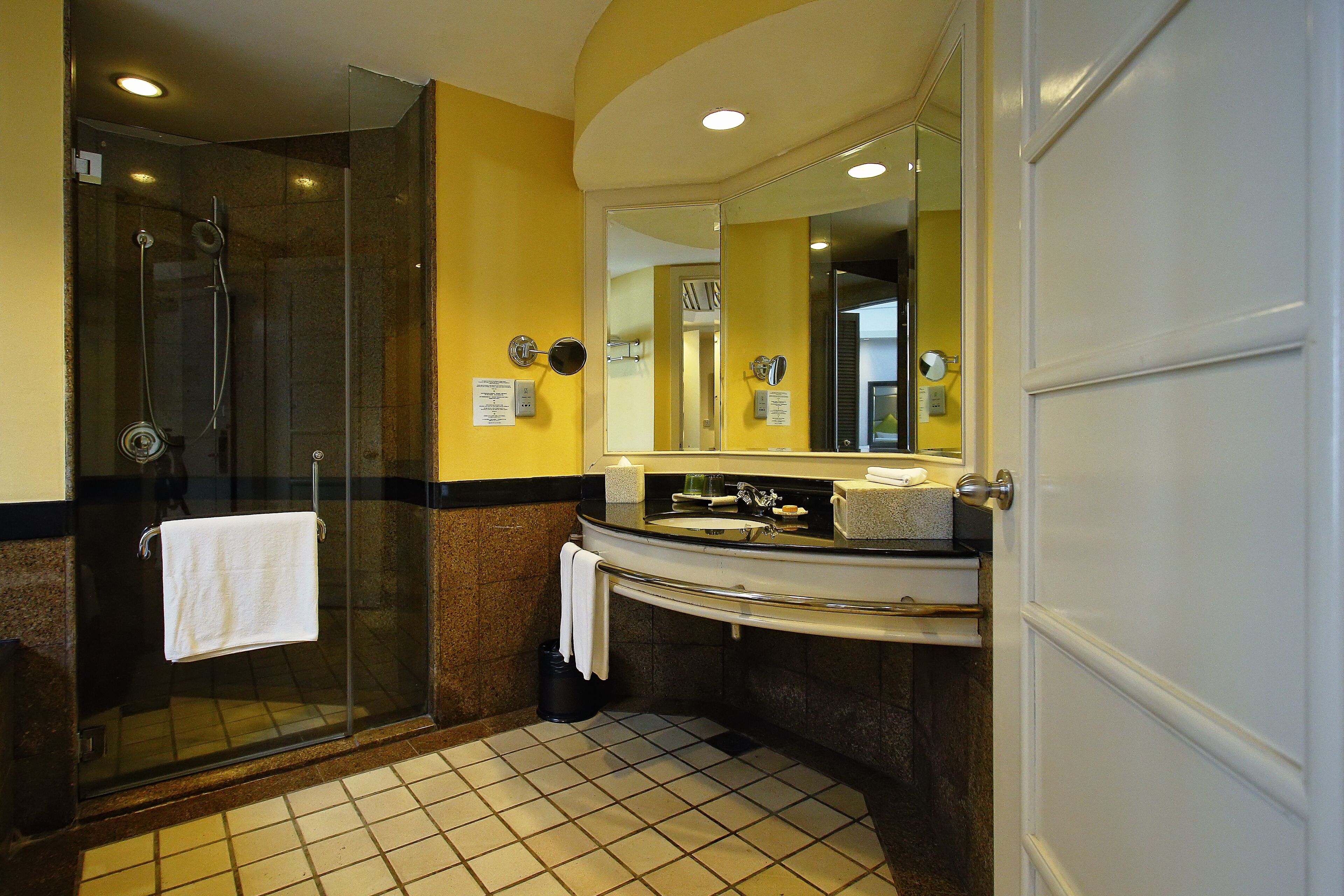 A bathroom with a glass-enclosed shower, a sink with a mirror, and a tiled floor.