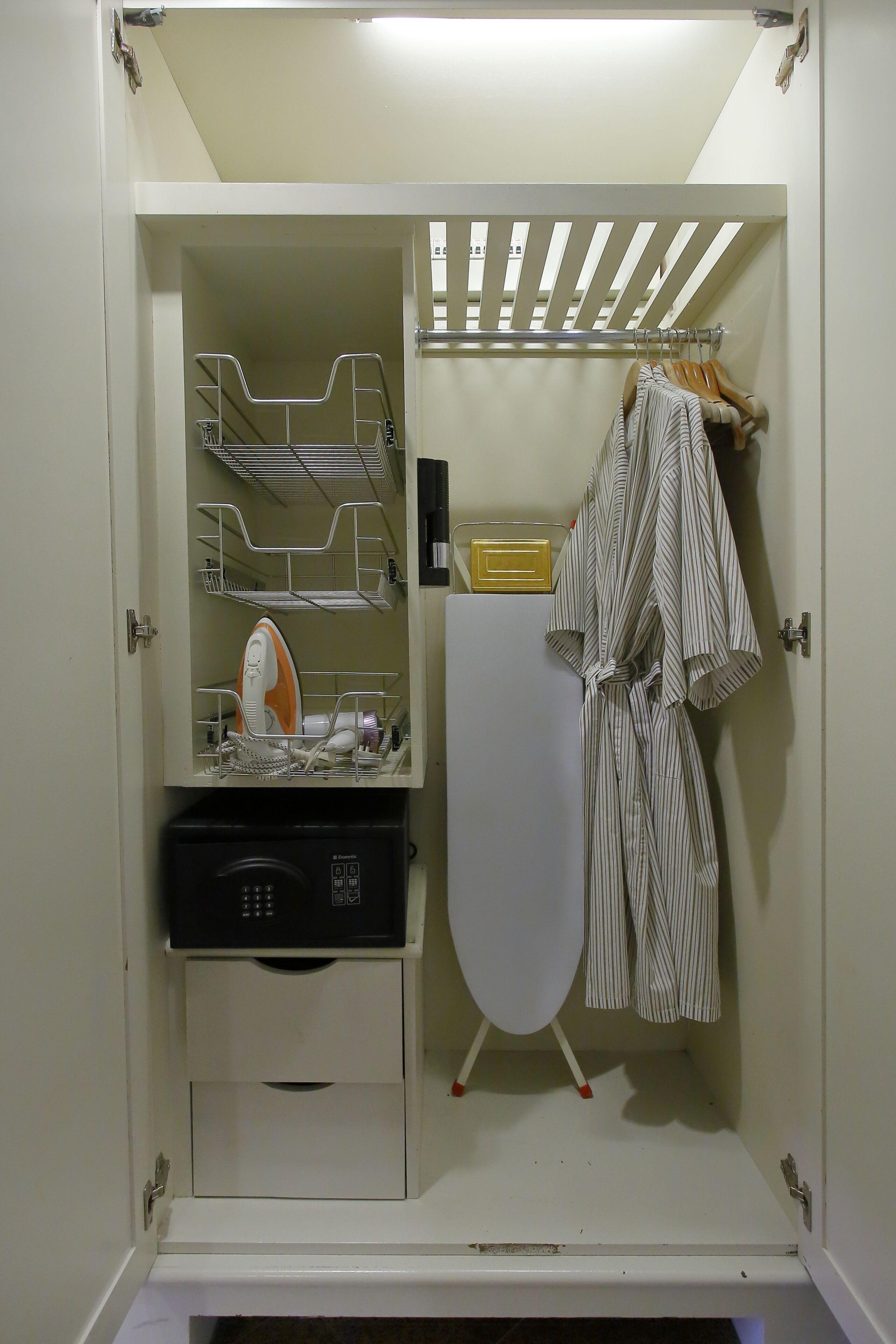 Ein kleines Zimmer mit integriertem Bügelbrett, einem kleinen Stauraumschrank und einer Kleiderstange.
