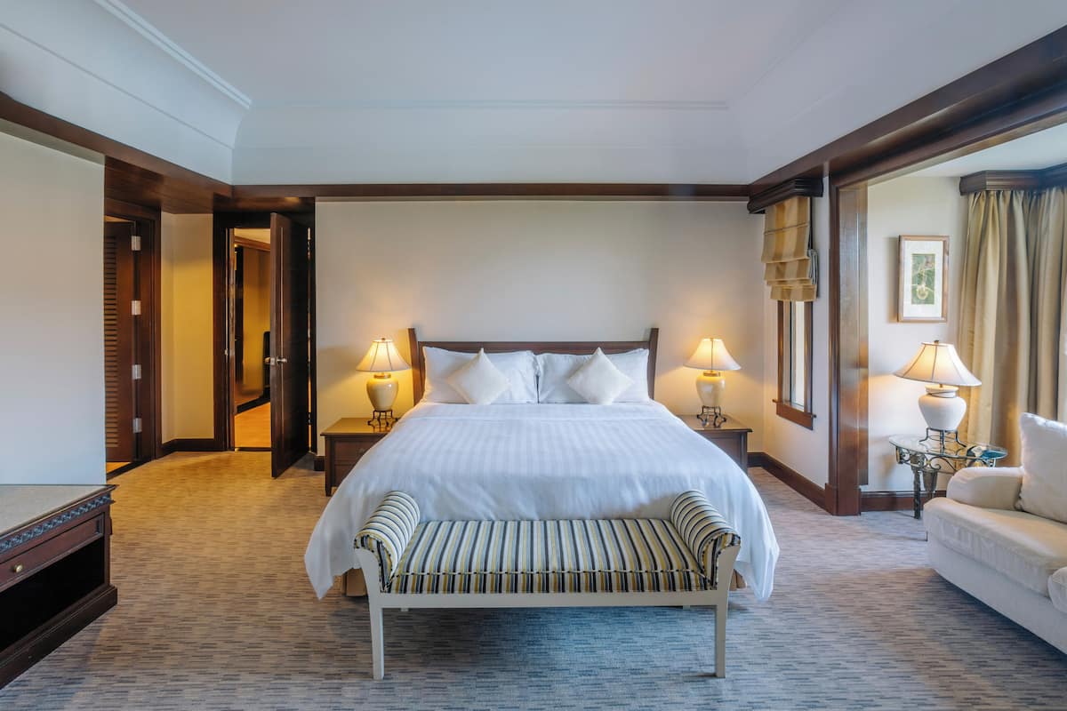 A hotel room with a large bed, two bedside tables with lamps, a bench, and a sofa.