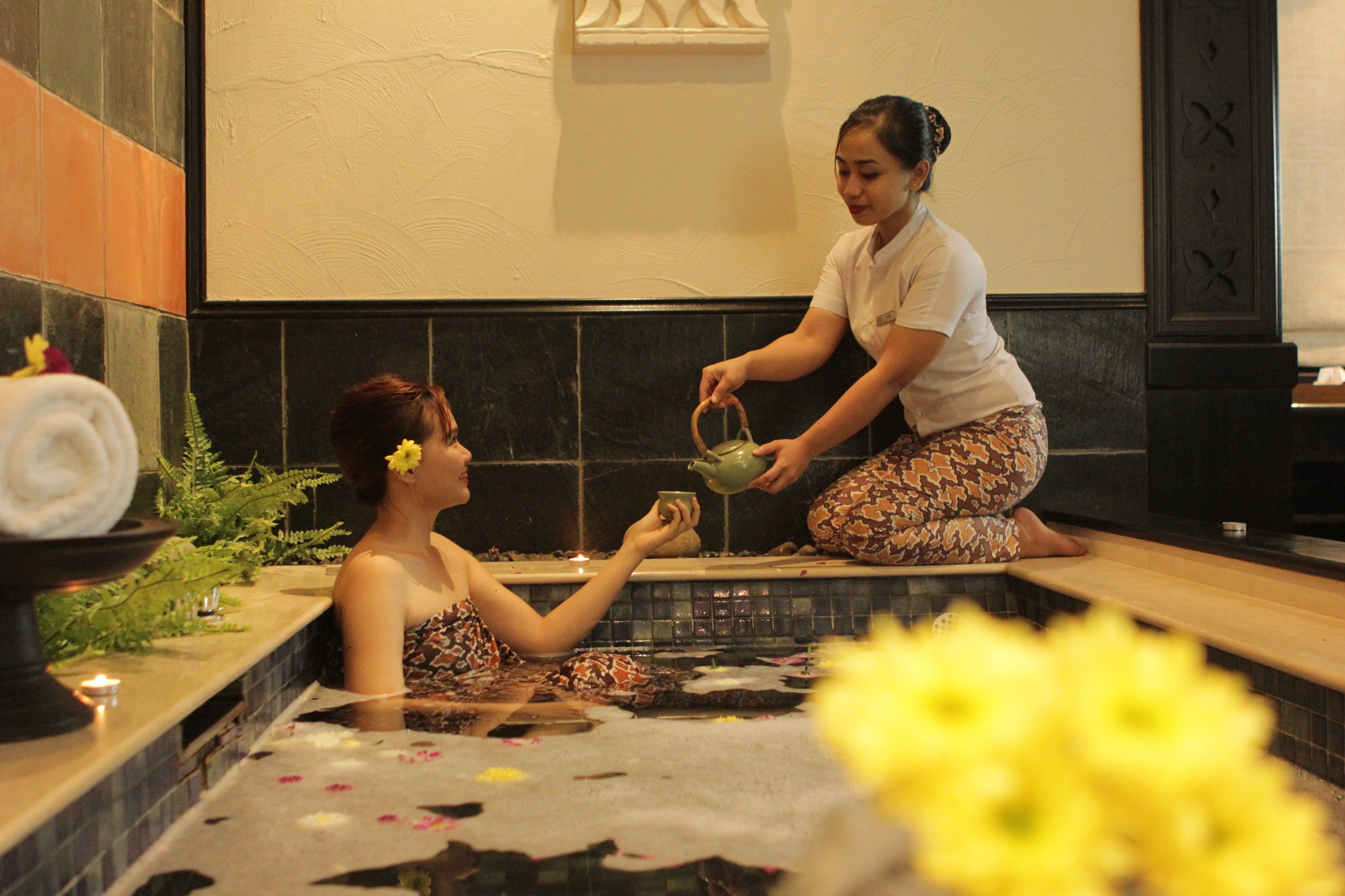A person in a bathtub receiving a drink from another person.
