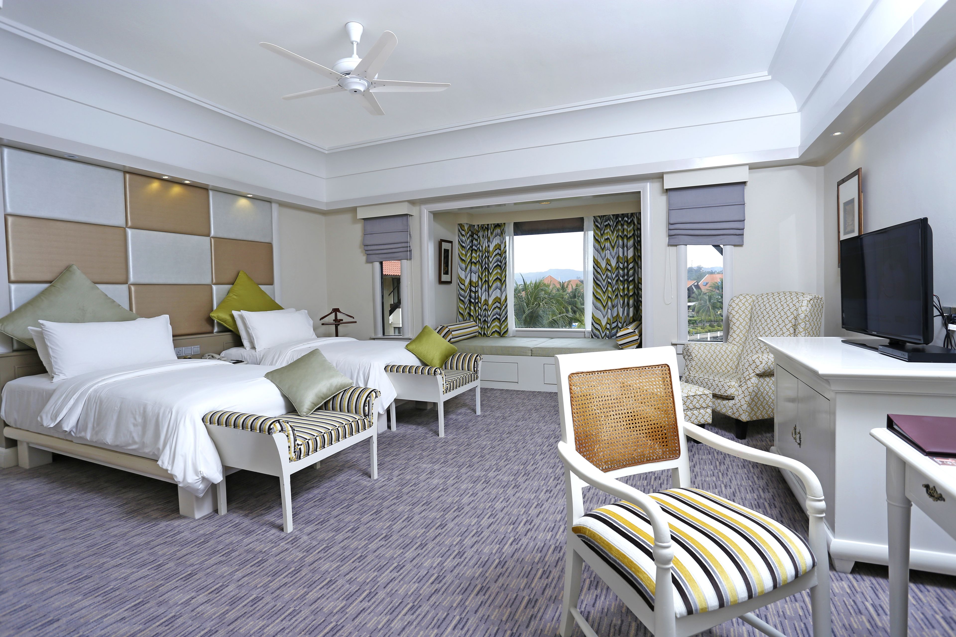 A hotel room with a bed, two bedside tables, a desk, a chair, a television, and a window with curtains.